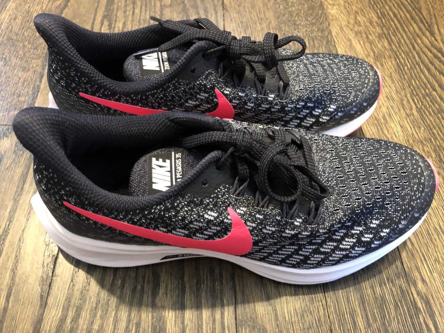 A pair of black and red nike shoes on top of a wooden floor.