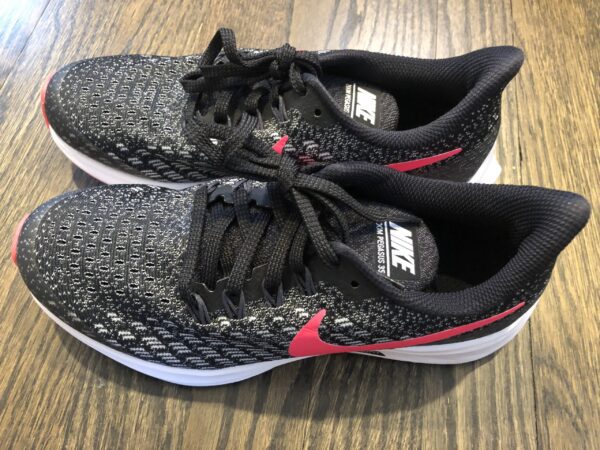A pair of black and red nike shoes on top of a wooden floor.