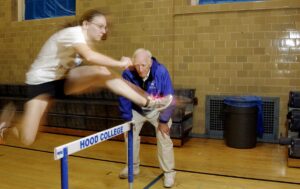 A man and woman jumping over an obstacle.