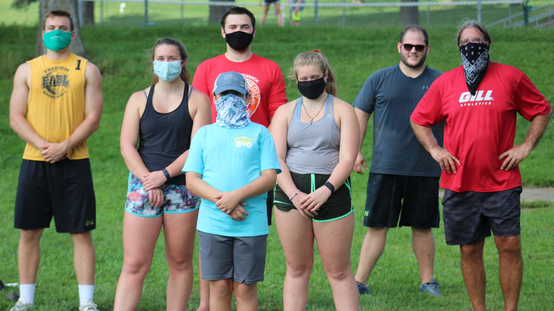 A group of people standing in the grass wearing masks.