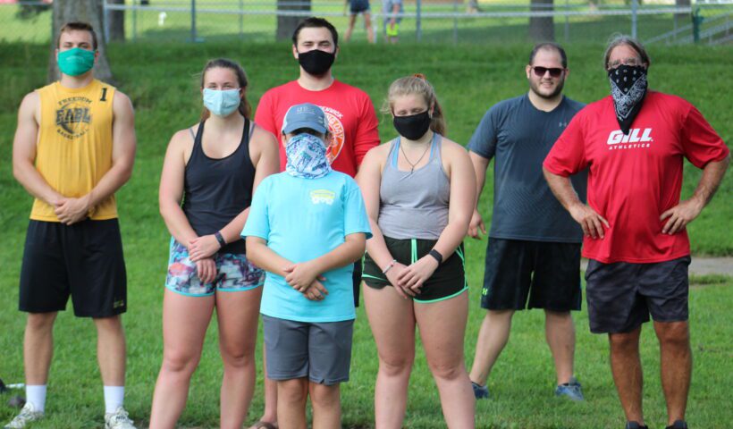 A group of people standing in the grass wearing masks.