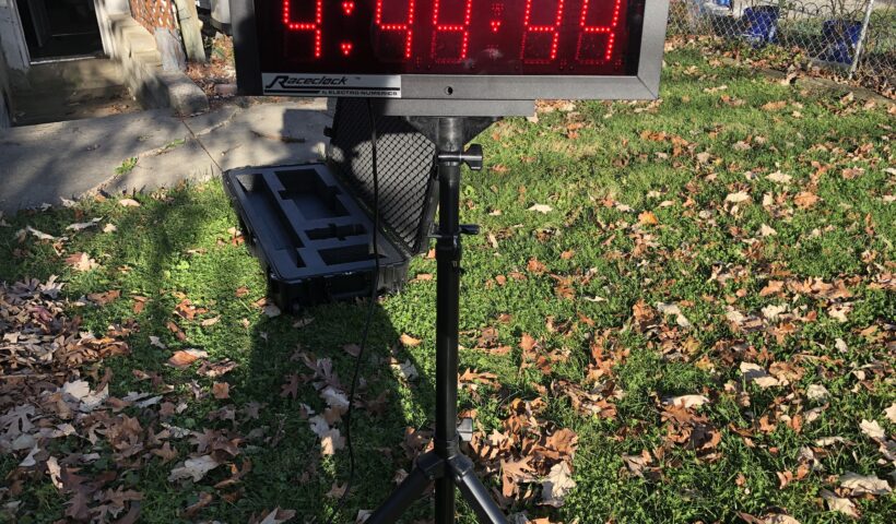 A digital clock on top of a tripod in the grass.