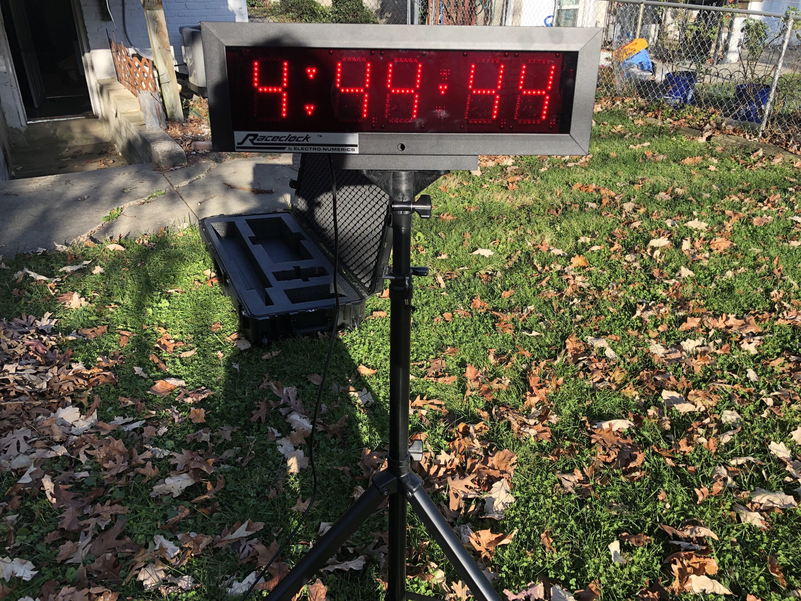 A digital clock on top of a tripod in the grass.