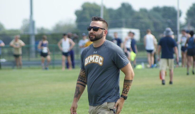 A man with tattoos walking across the grass.