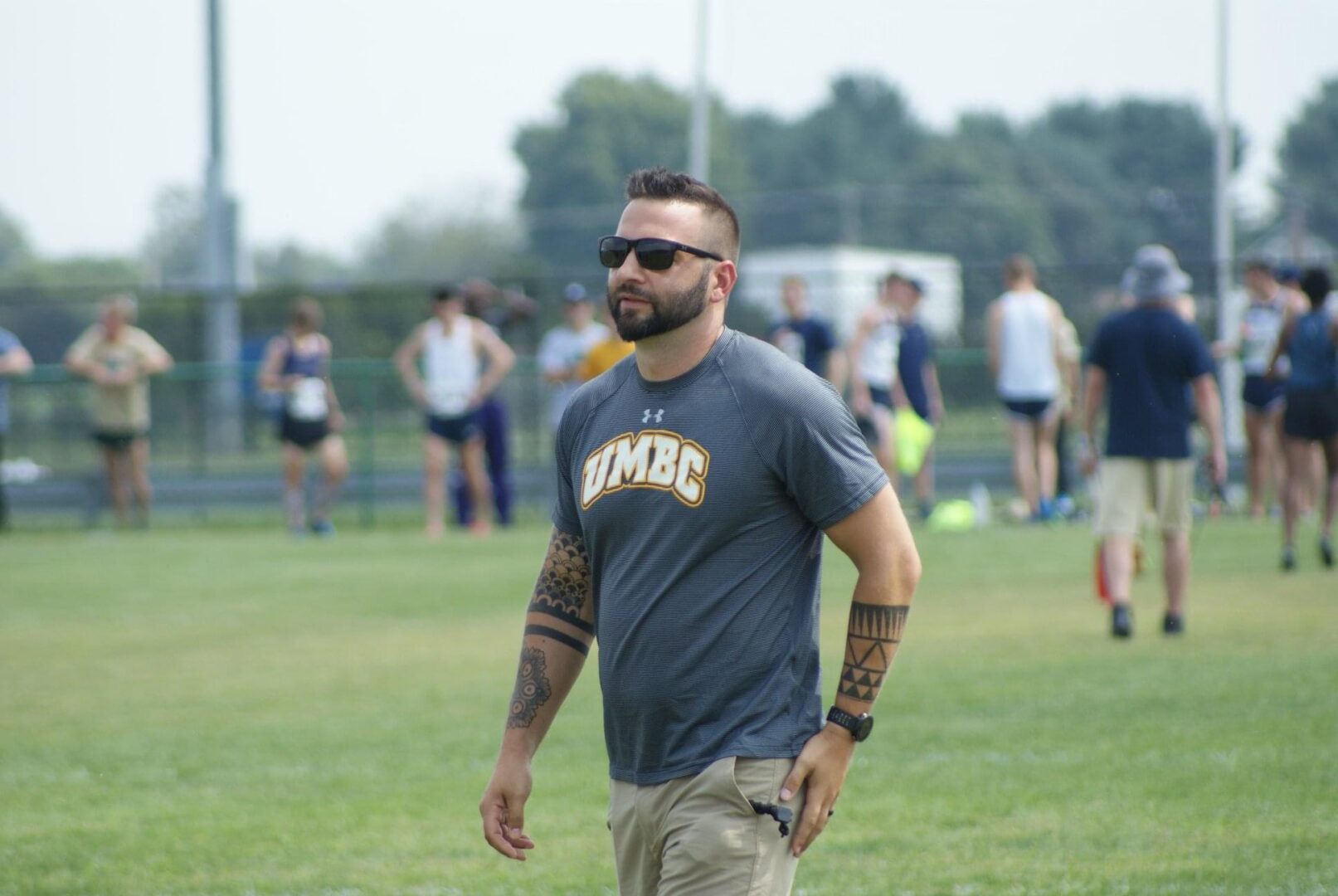 A man with tattoos walking across the grass.