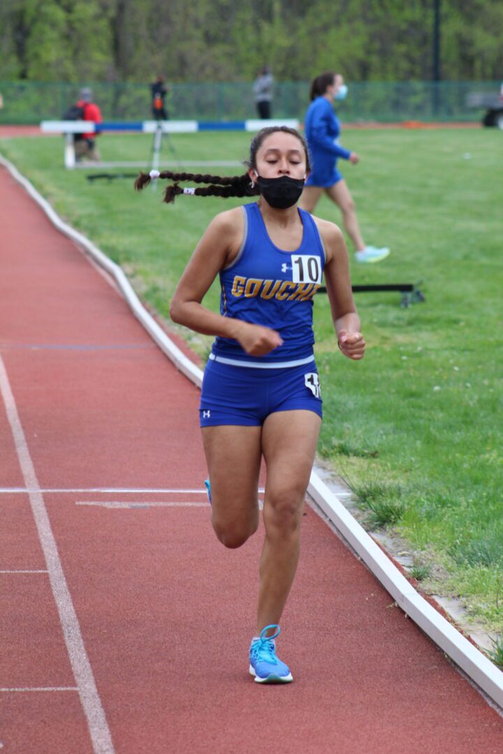 A girl running on the track wearing blue shorts and a black mask.