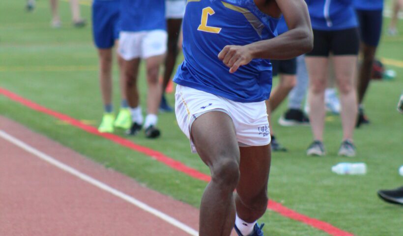 A man running on the track with other people watching.