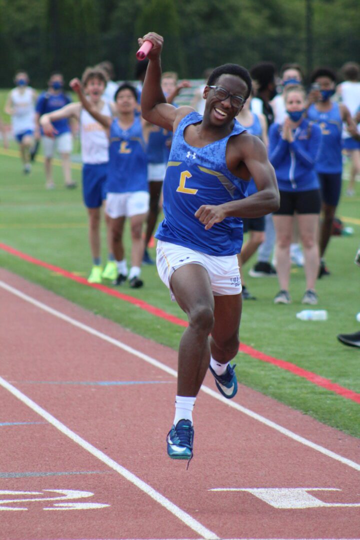 A man running on the track with other people watching.