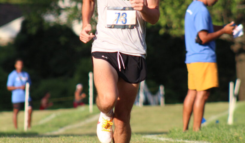 A man running on the grass with other people watching.