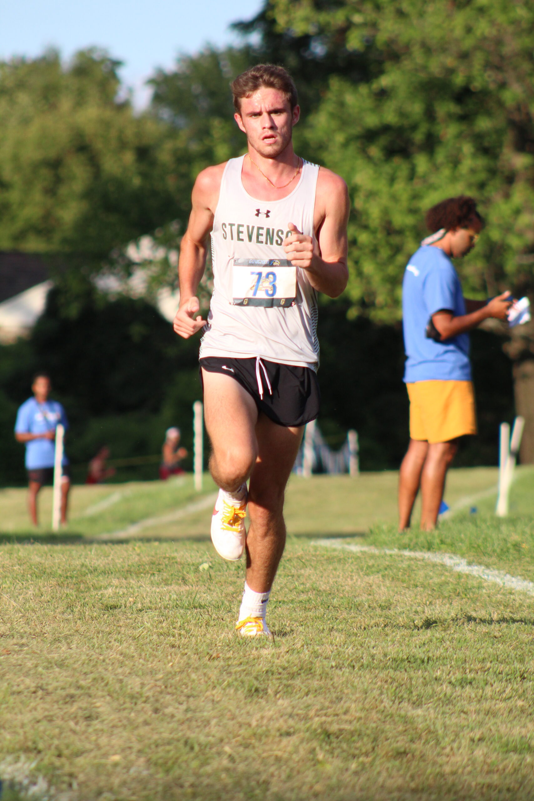 A man running on the grass with other people watching.