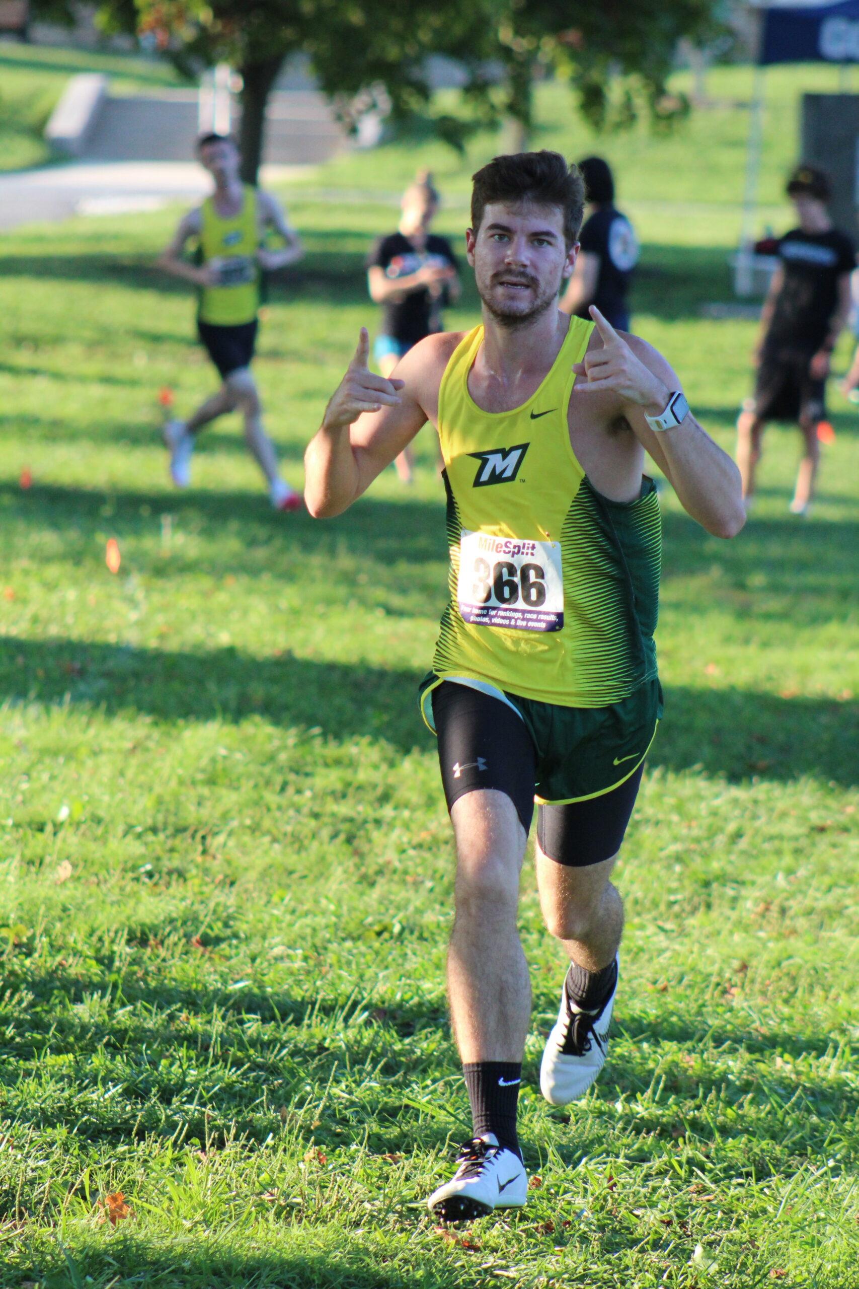 A man running in the grass with his thumb up.