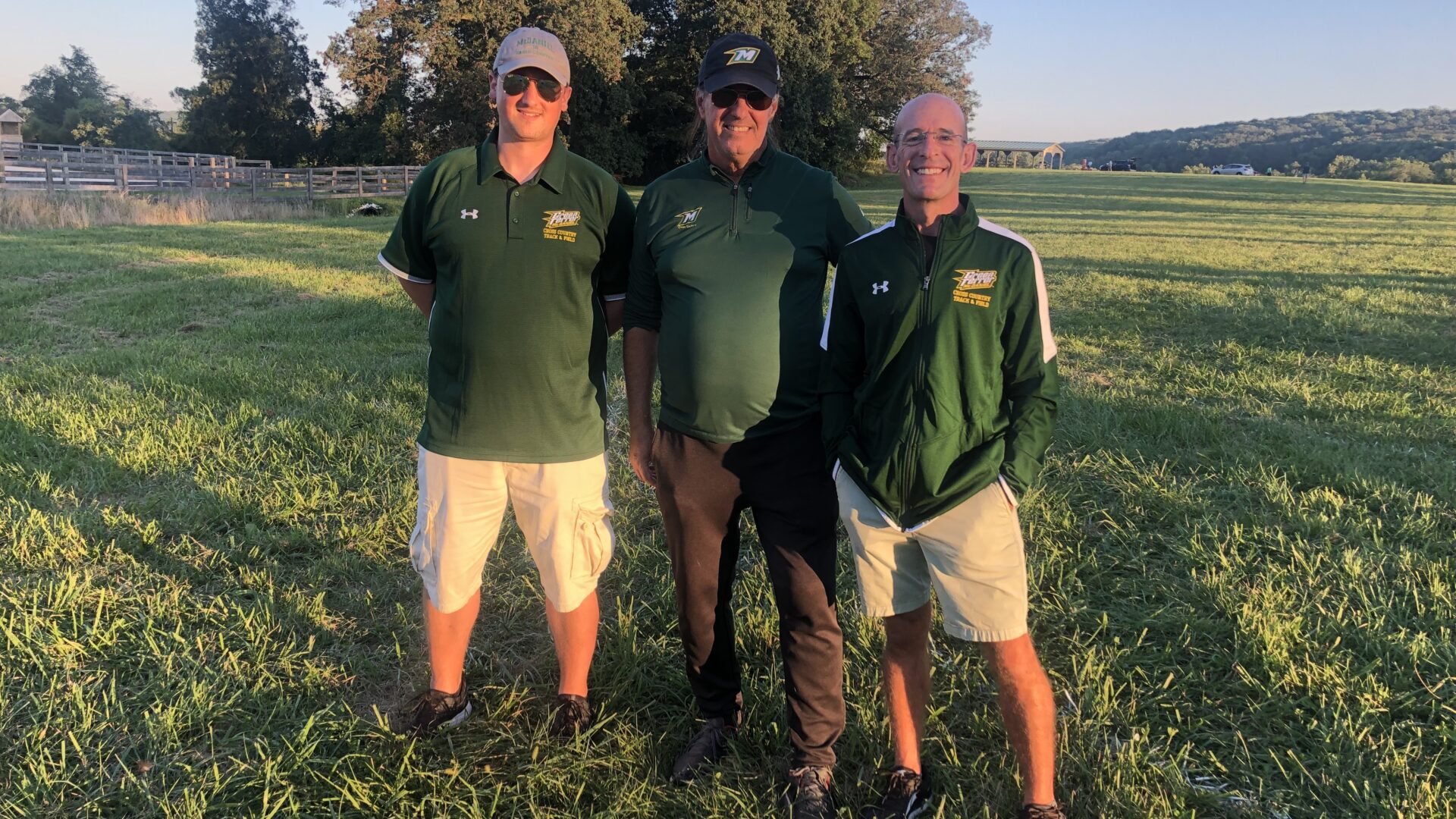 Three men standing in a field with trees behind them.