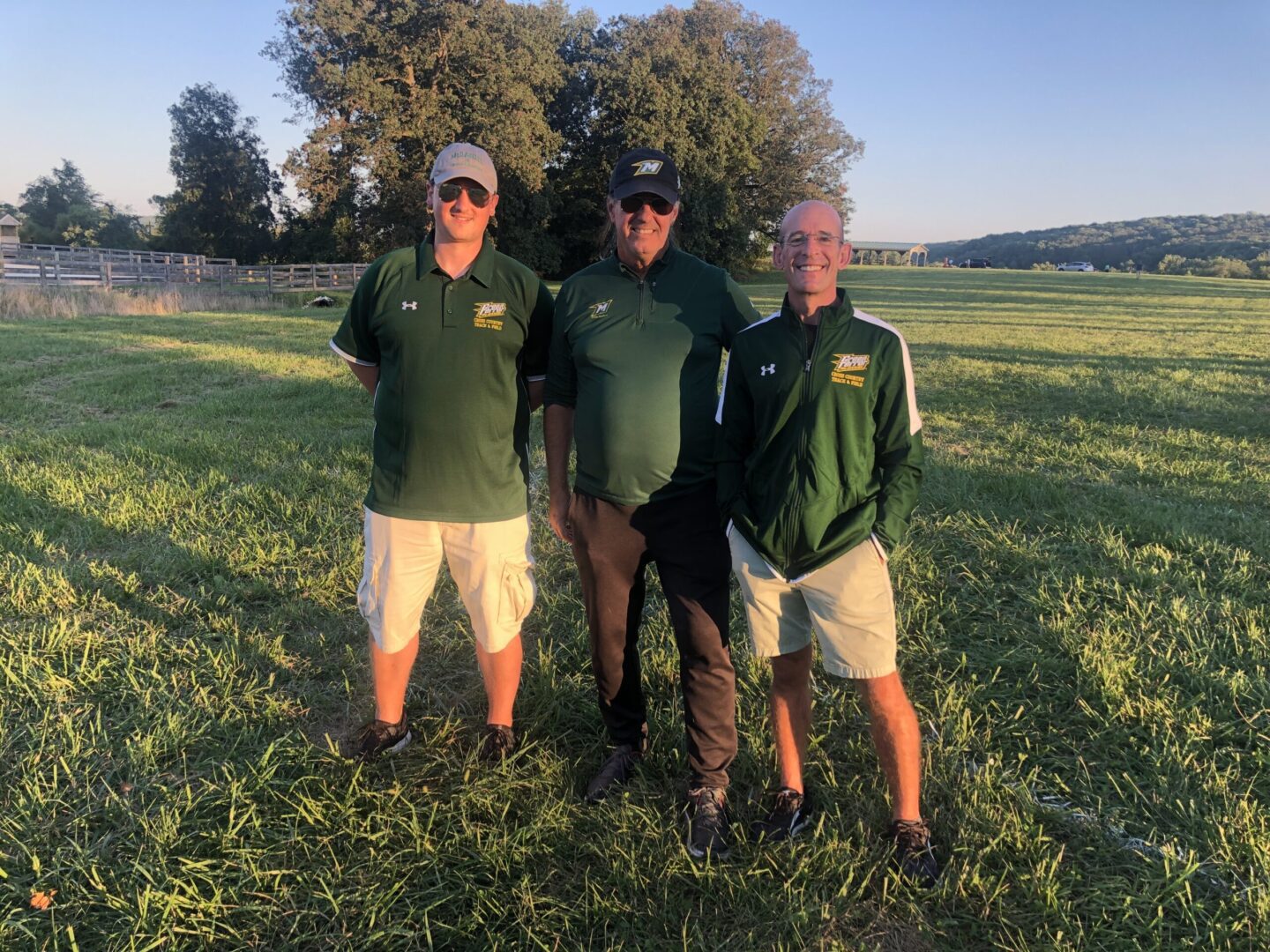 Three men standing in a field with trees behind them.