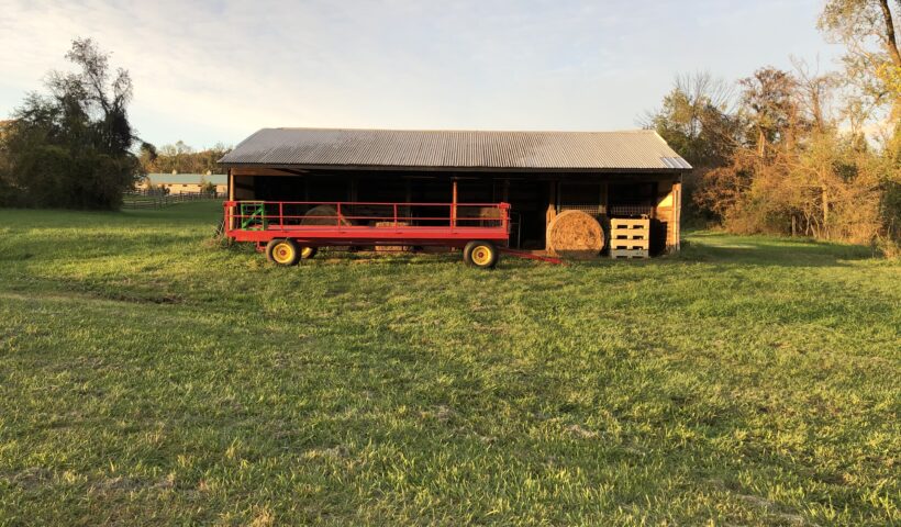 A red truck parked in front of a barn.