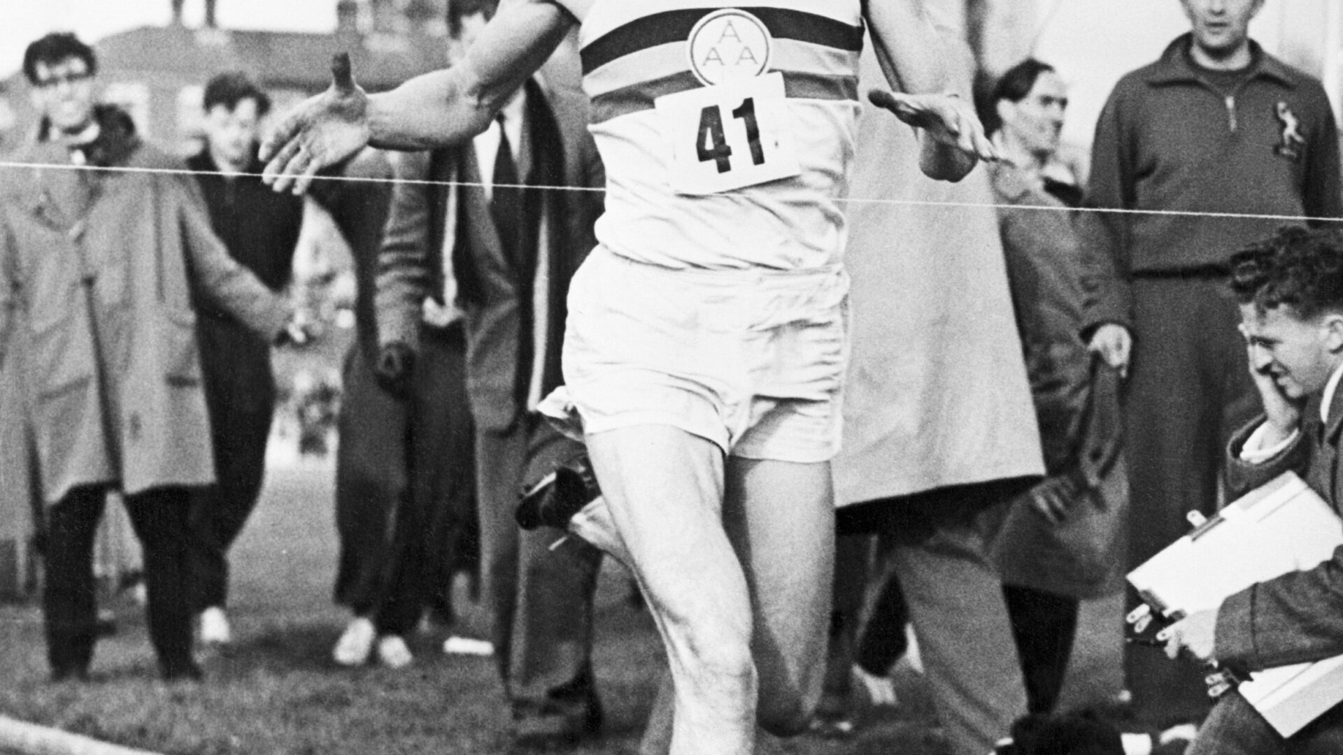 A man running on the track with people watching.