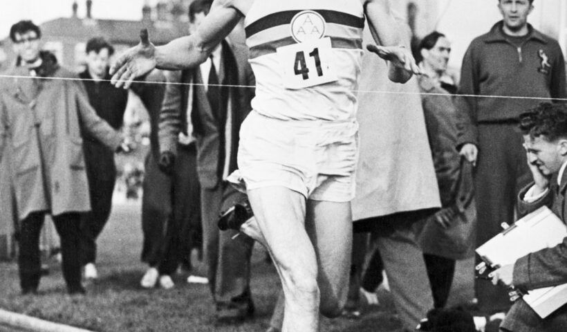 A man running on the track with people watching.