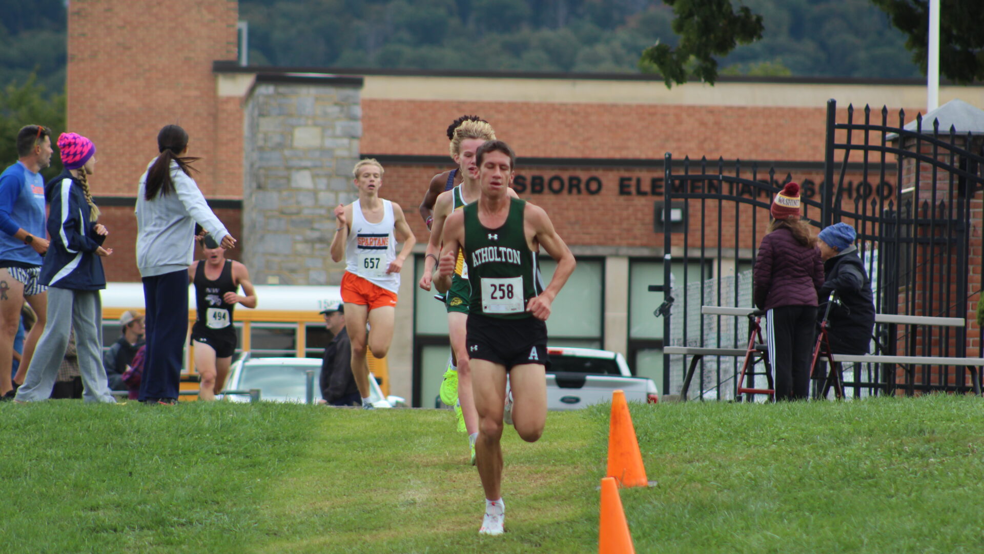 A person running in the grass near orange cones.