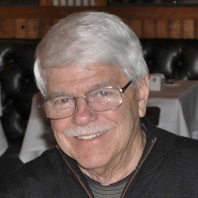 A man with white hair and glasses smiling.