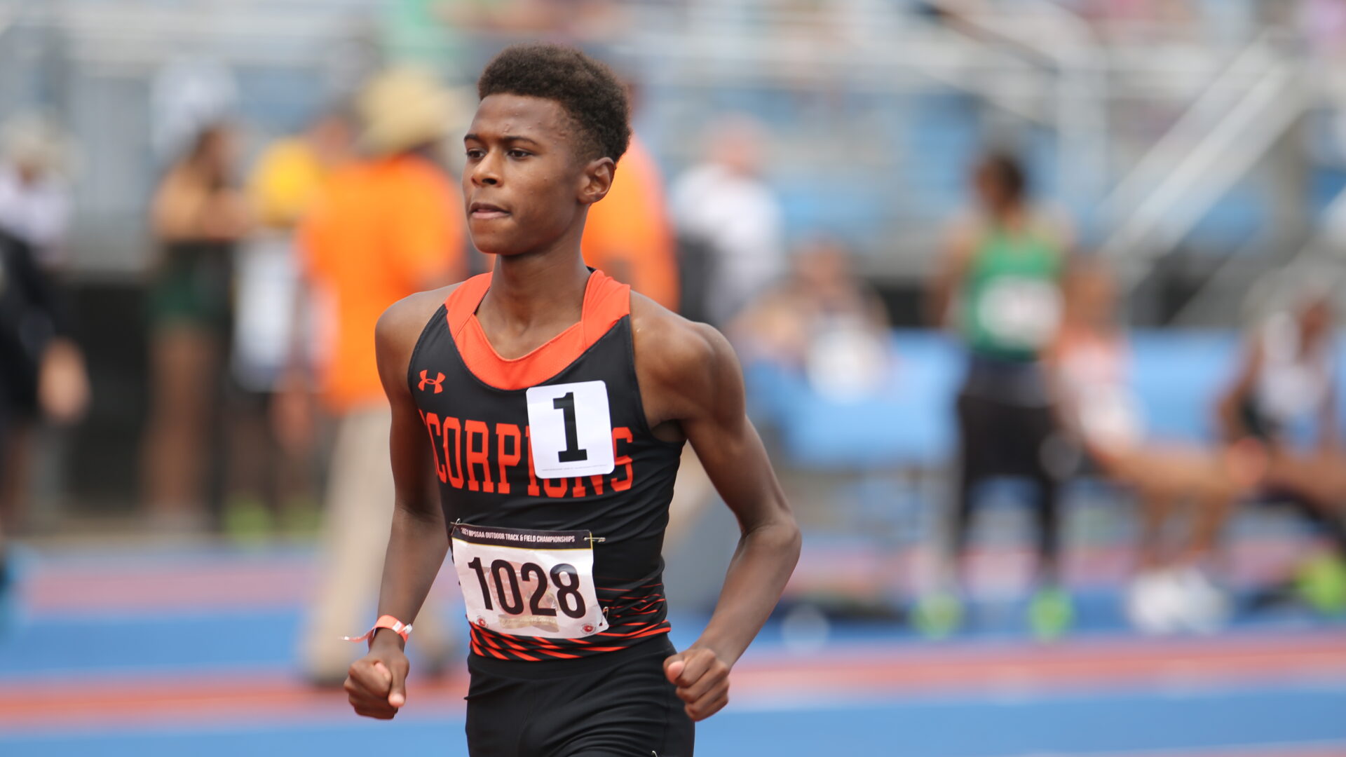 A young man running on the track in front of an audience.