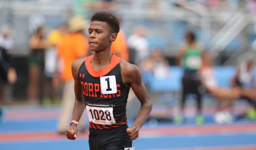 A young man running on the track in front of an audience.