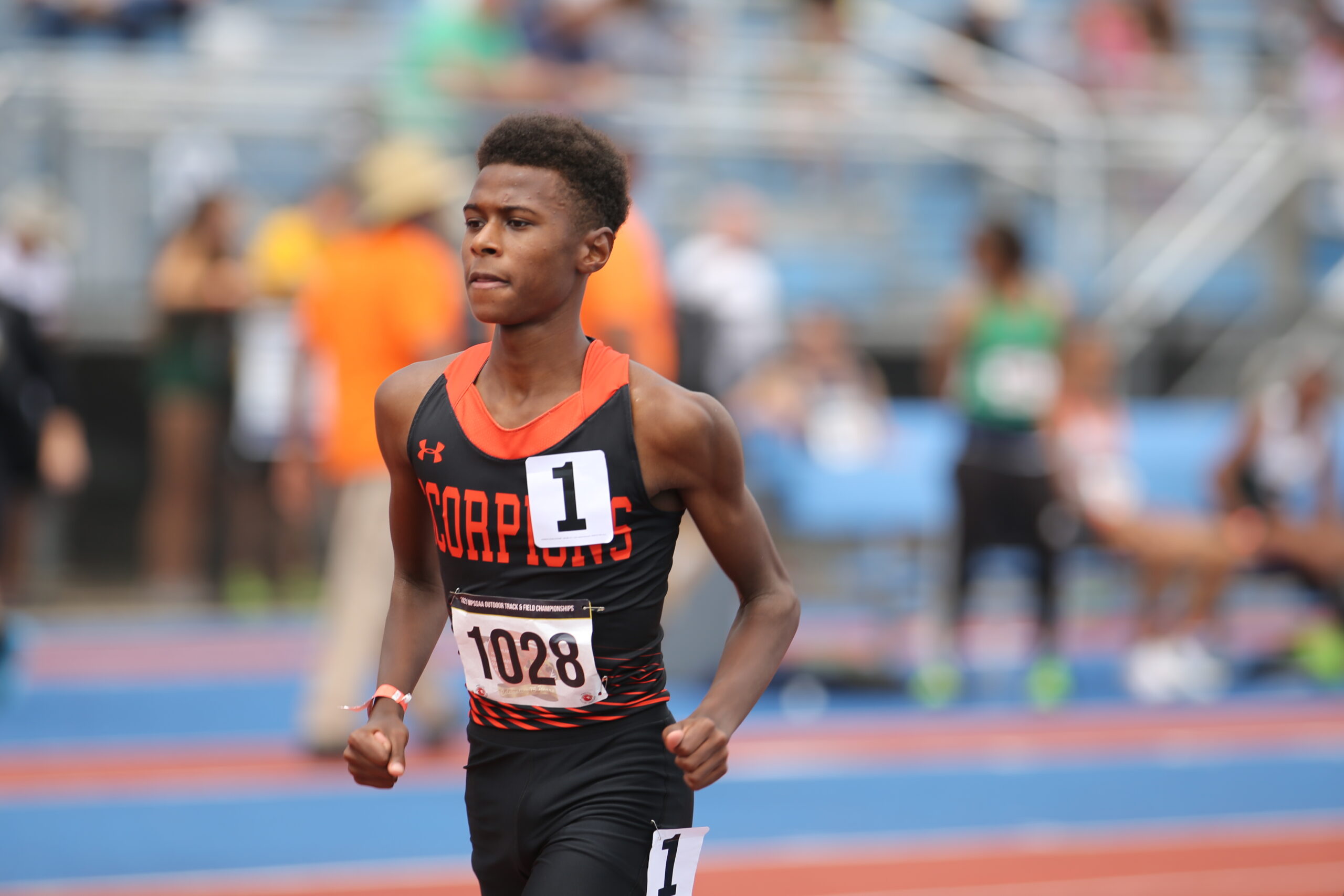 A young man running on the track in front of an audience.