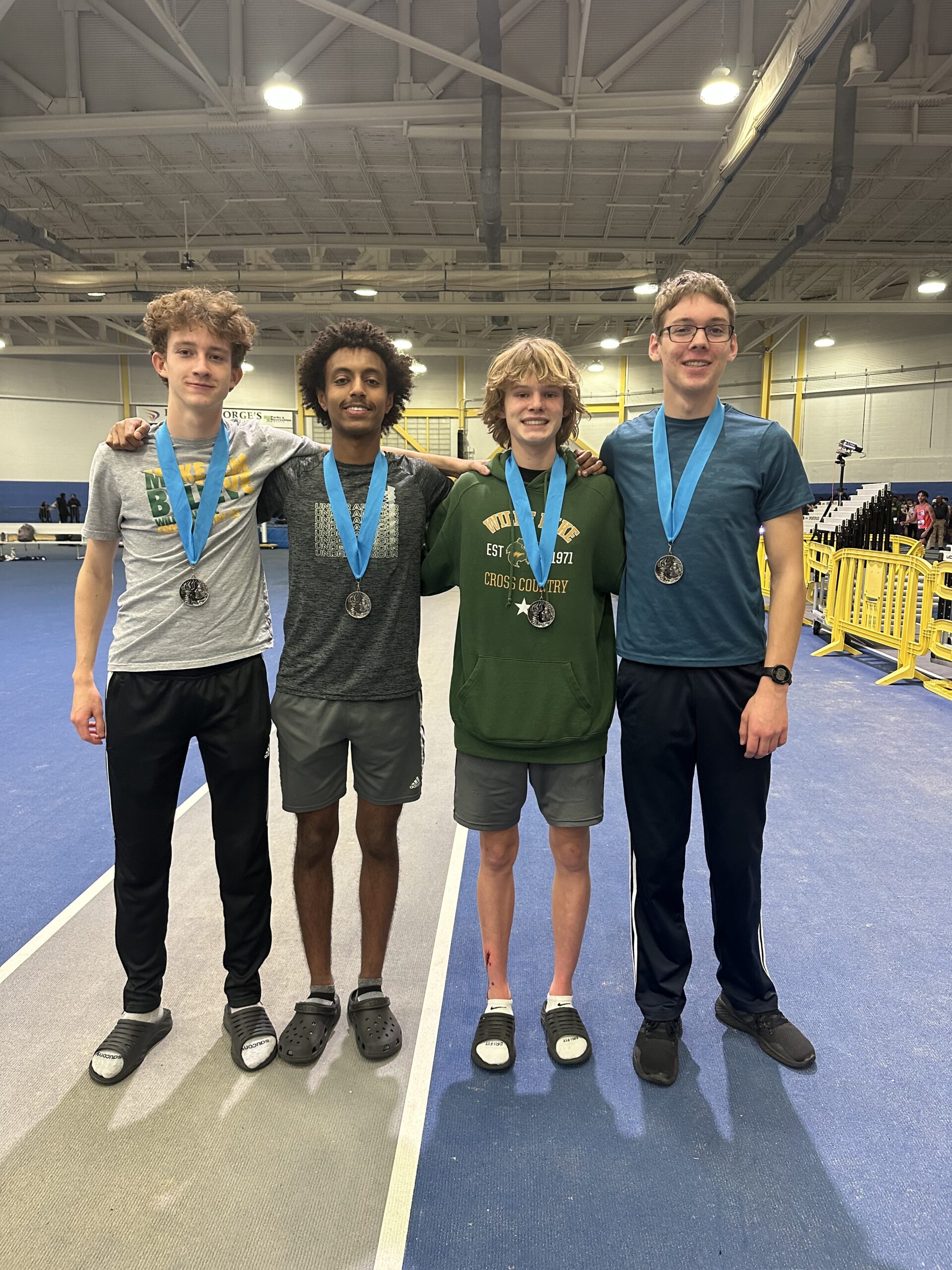 Four boys standing next to each other with medals around their necks.
